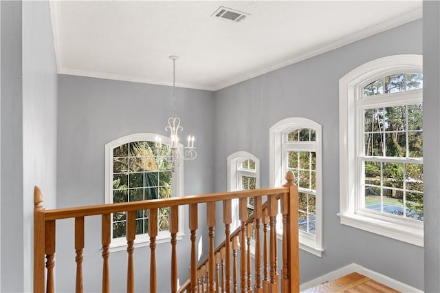 hallway with ornamental molding, a healthy amount of sunlight, and an inviting chandelier