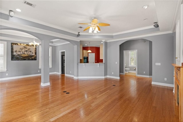 unfurnished living room featuring ceiling fan with notable chandelier, light wood-type flooring, a tray ceiling, and ornamental molding