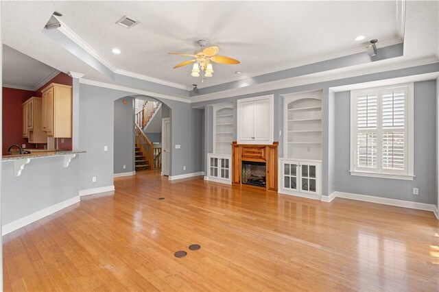 unfurnished living room featuring a raised ceiling, sink, ceiling fan, light wood-type flooring, and ornamental molding