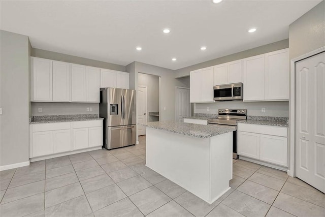 kitchen with light tile patterned flooring, light stone counters, white cabinetry, a kitchen island, and stainless steel appliances