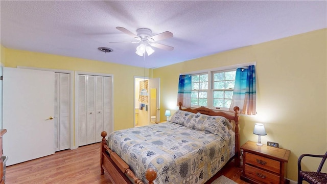 bedroom with two closets, wood finished floors, a ceiling fan, and a textured ceiling