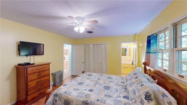 bedroom with connected bathroom, multiple closets, light wood finished floors, and a ceiling fan