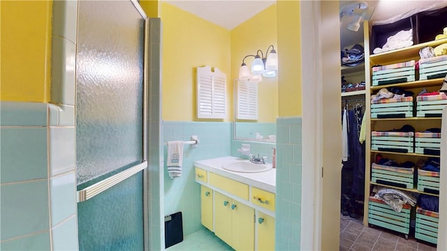 bathroom featuring a walk in closet, tile walls, a stall shower, a wainscoted wall, and vanity