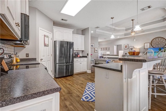 kitchen with a tray ceiling, visible vents, dark countertops, and freestanding refrigerator