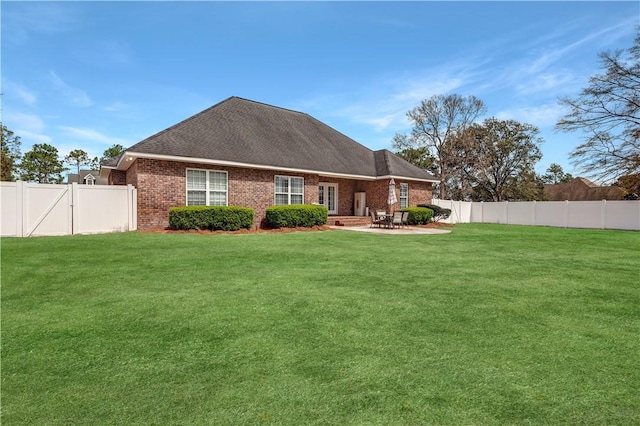 rear view of house with brick siding, a fenced backyard, a lawn, and a patio