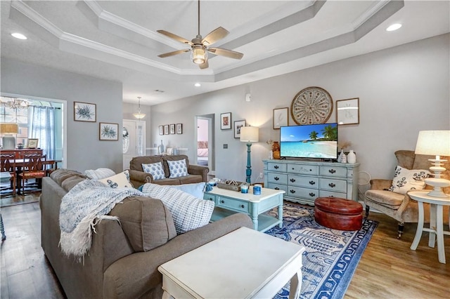 living area with light wood-style flooring, a ceiling fan, ornamental molding, recessed lighting, and a raised ceiling