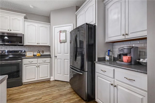 kitchen featuring light wood-style floors, stainless steel appliances, dark countertops, and white cabinetry