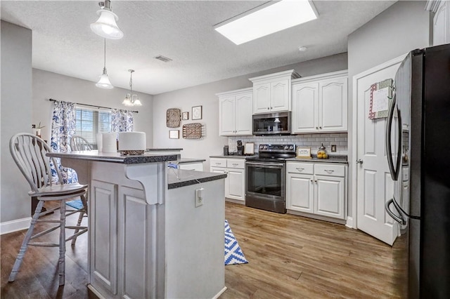 kitchen with visible vents, stainless steel appliances, white cabinetry, dark countertops, and a kitchen breakfast bar