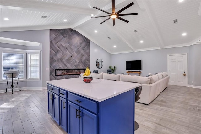 kitchen with a tile fireplace, vaulted ceiling with beams, light hardwood / wood-style floors, blue cabinetry, and a kitchen island