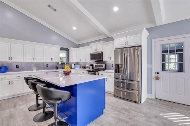 kitchen featuring light hardwood / wood-style flooring, vaulted ceiling with beams, appliances with stainless steel finishes, a kitchen island, and white cabinetry