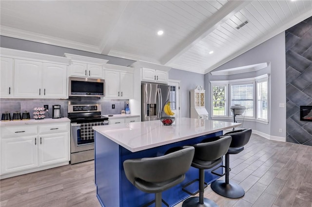 kitchen with vaulted ceiling with beams, white cabinets, light hardwood / wood-style floors, a kitchen island, and appliances with stainless steel finishes