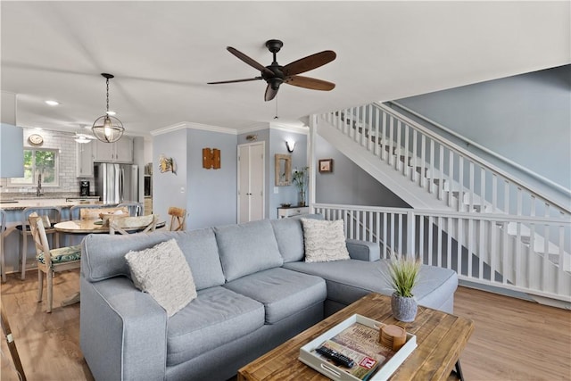 living room featuring ceiling fan, sink, ornamental molding, and light wood-type flooring