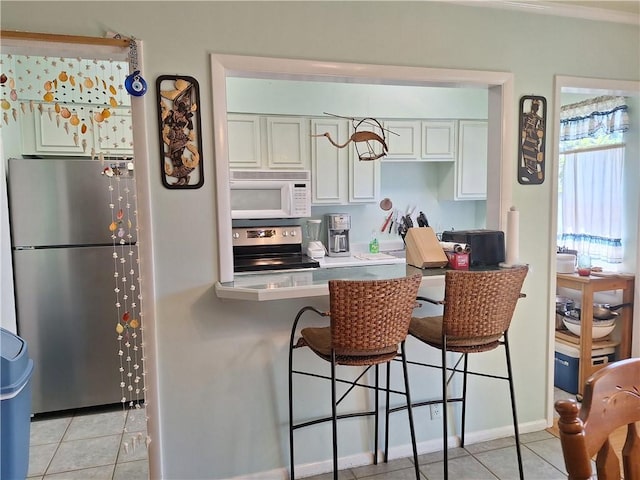 kitchen with a kitchen breakfast bar, white cabinetry, light tile patterned floors, and appliances with stainless steel finishes