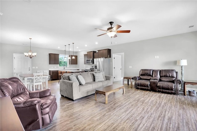 living room with light wood-type flooring, ceiling fan with notable chandelier, and sink