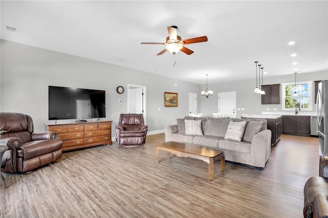 living room with hardwood / wood-style floors, ceiling fan with notable chandelier, and sink