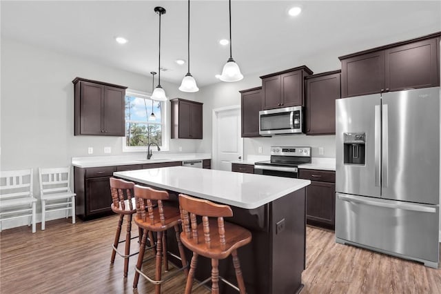 kitchen featuring sink, a center island, stainless steel appliances, decorative light fixtures, and a kitchen bar