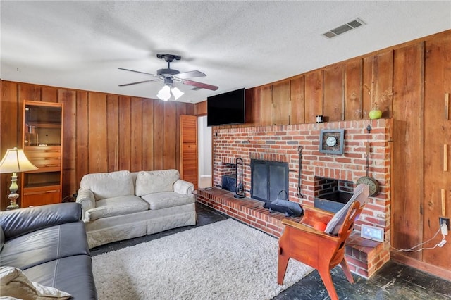 living room with a textured ceiling, a brick fireplace, ceiling fan, and wood walls