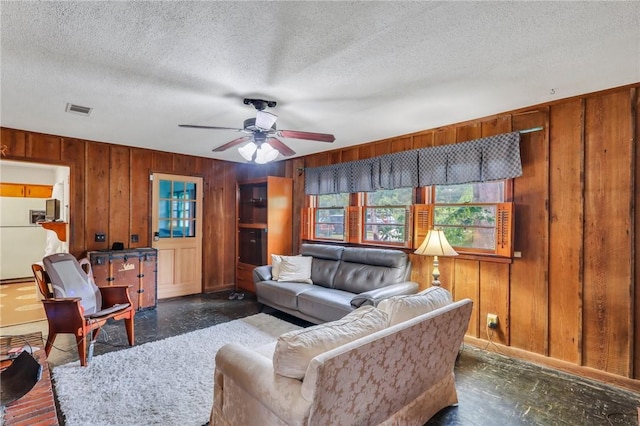 living room with a textured ceiling, ceiling fan, and wood walls