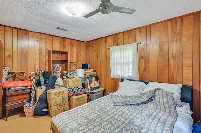 carpeted bedroom with ceiling fan, wood walls, and a textured ceiling