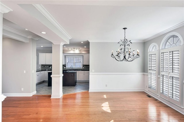 unfurnished dining area featuring light hardwood / wood-style floors, an inviting chandelier, ornamental molding, and sink