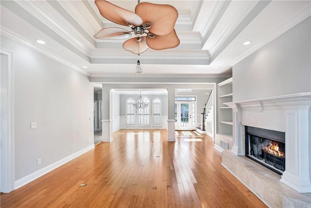 unfurnished living room with built in features, light wood-type flooring, ornamental molding, and a tray ceiling