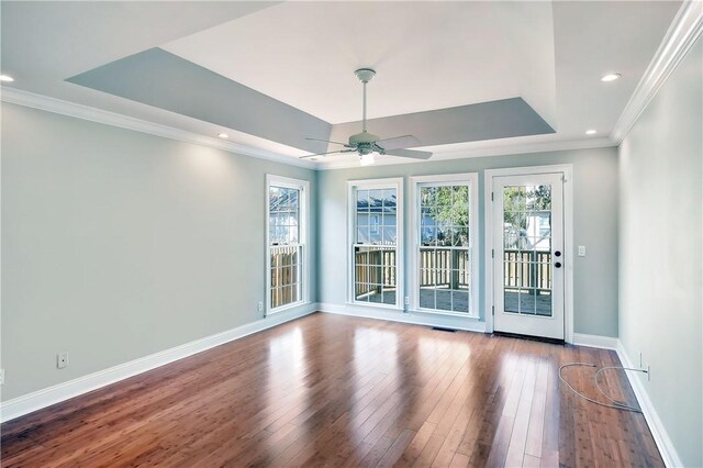 unfurnished room with a healthy amount of sunlight, a raised ceiling, wood-type flooring, and crown molding