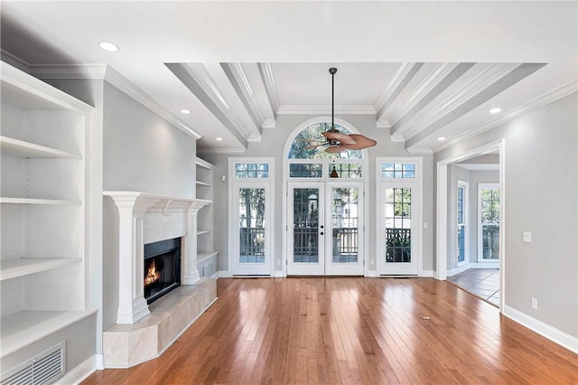 unfurnished living room featuring ceiling fan, built in features, wood-type flooring, a fireplace, and ornamental molding