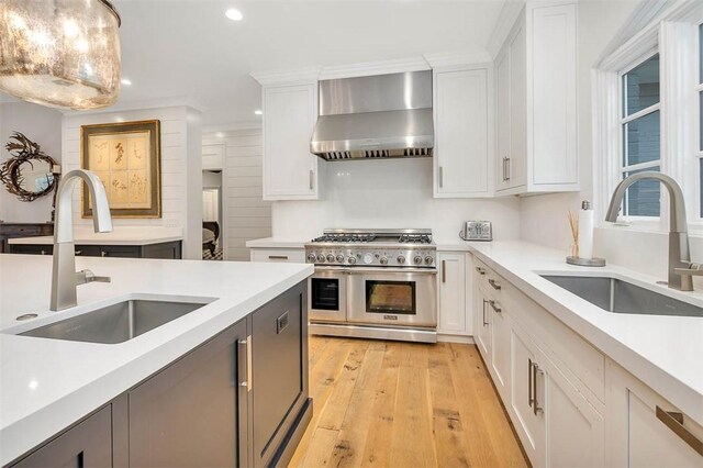 kitchen with wall chimney exhaust hood, double oven range, white cabinetry, and sink