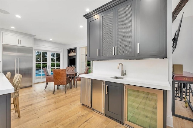 kitchen with built in refrigerator, sink, beverage cooler, and light hardwood / wood-style flooring