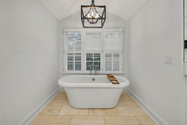 bathroom with tile patterned flooring, vaulted ceiling, a notable chandelier, and a tub