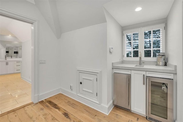 bar with white cabinetry, light hardwood / wood-style flooring, beverage cooler, and sink