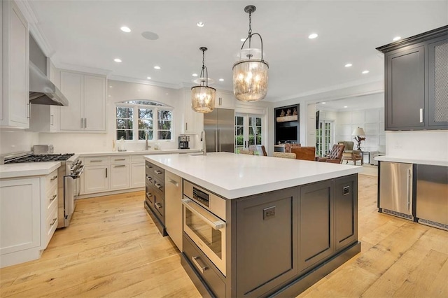 kitchen with wall chimney range hood, premium appliances, light hardwood / wood-style flooring, a spacious island, and white cabinets