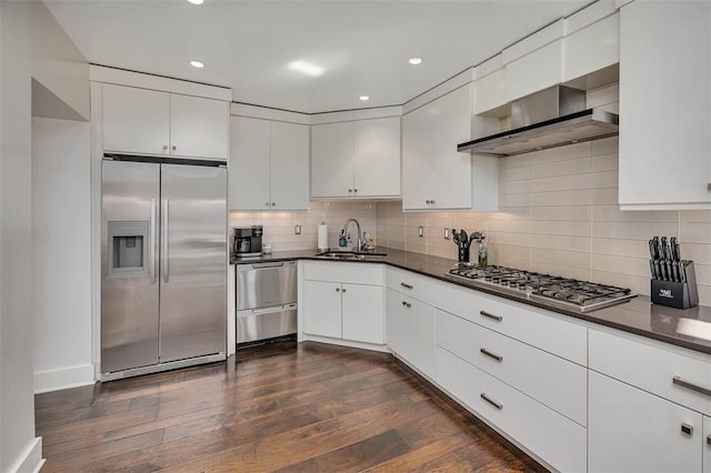 kitchen featuring stainless steel appliances, wall chimney exhaust hood, dark countertops, and a sink