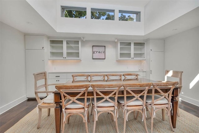 dining room featuring dark wood-style floors, a high ceiling, and baseboards