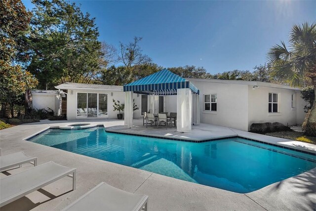 rear view of house with a pool with connected hot tub, a patio area, and stucco siding