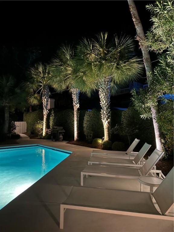 pool at night with a patio, a grill, and an outdoor pool