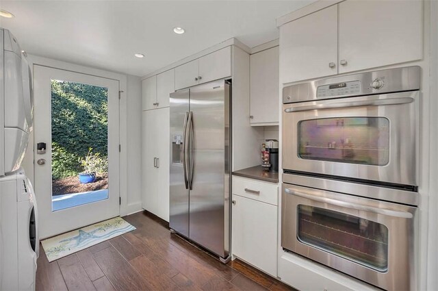 kitchen featuring appliances with stainless steel finishes, stacked washer / drying machine, dark wood-type flooring, and plenty of natural light