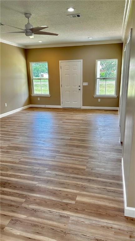 empty room with ceiling fan, light wood-type flooring, crown molding, and a wealth of natural light