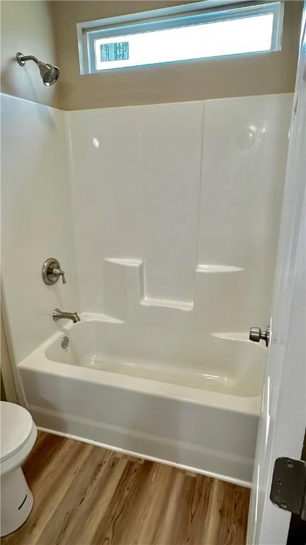 bathroom with wood-type flooring, shower / bath combination, toilet, and a healthy amount of sunlight