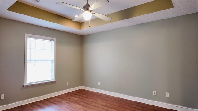 unfurnished room featuring ceiling fan, wood-type flooring, and a tray ceiling