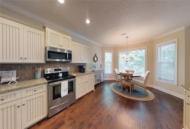 kitchen with dark wood-type flooring, appliances with stainless steel finishes, hanging light fixtures, backsplash, and cream cabinetry