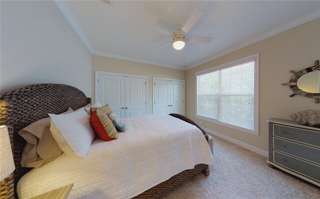 bedroom with light carpet, ceiling fan, ornamental molding, and multiple closets