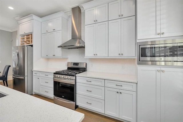 kitchen featuring tasteful backsplash, crown molding, wall chimney range hood, stainless steel appliances, and white cabinetry