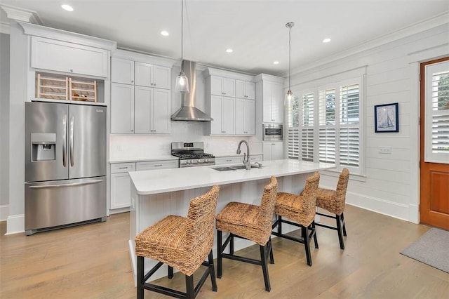 kitchen featuring light wood-style flooring, a sink, wall chimney range hood, stainless steel appliances, and light countertops