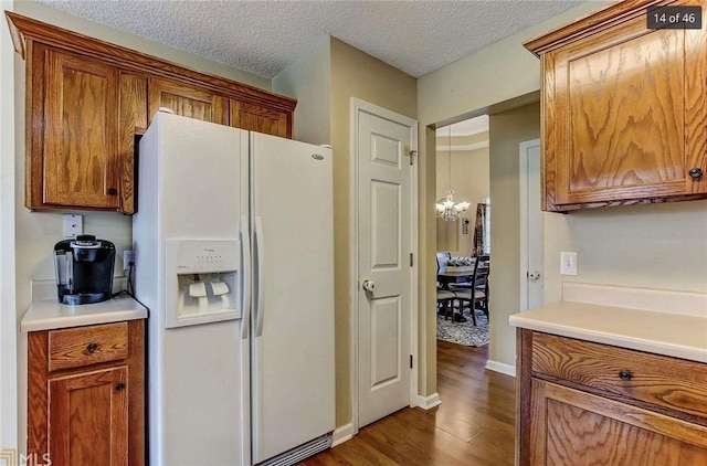 kitchen featuring brown cabinetry, dark wood-style flooring, light countertops, white fridge with ice dispenser, and a textured ceiling