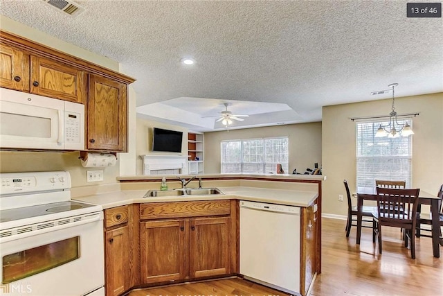 kitchen featuring visible vents, brown cabinets, a peninsula, white appliances, and a sink