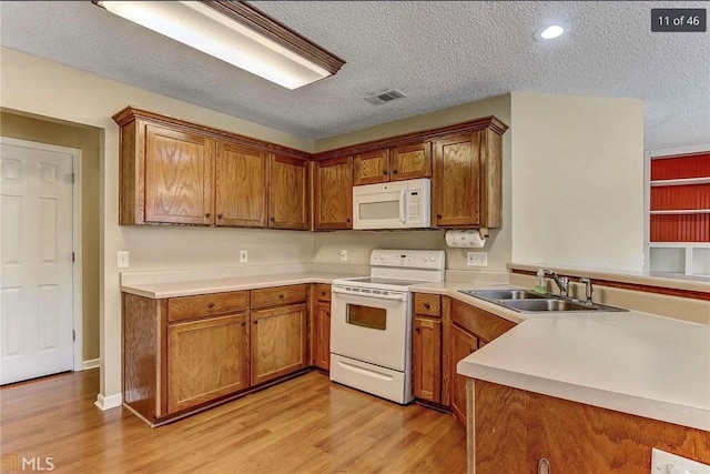 kitchen featuring a sink, visible vents, white appliances, and brown cabinets