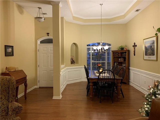 dining area featuring visible vents, a tray ceiling, dark wood-style flooring, a decorative wall, and a chandelier