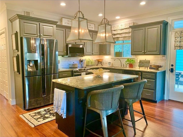 kitchen with sink, hanging light fixtures, hardwood / wood-style floors, a kitchen island, and appliances with stainless steel finishes