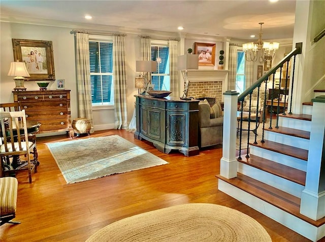 interior space with a chandelier, wood-type flooring, a brick fireplace, and crown molding